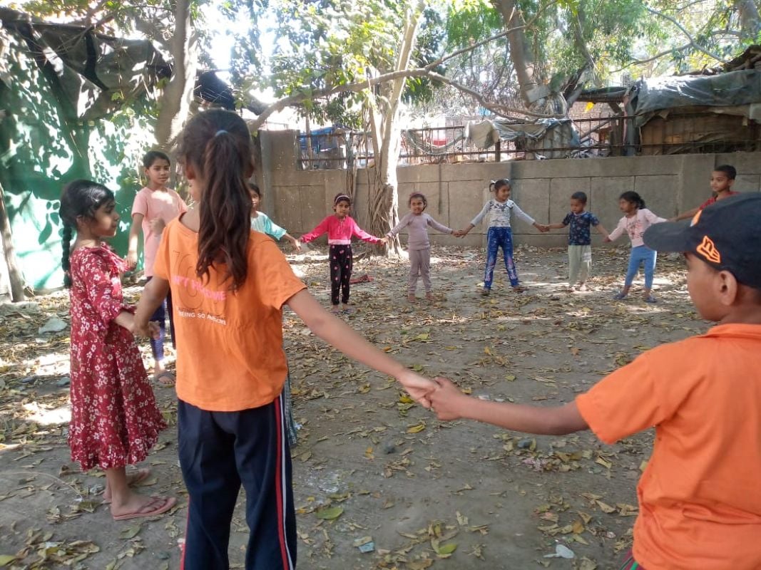 Children hold hands in a circle during an outdoor group activity at a Shikshadwar programme centre